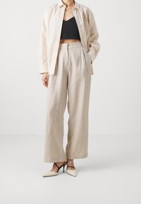 Beige linnebyxor med vida ben i kombination med en svart kort topp och krämfärgade klackskor med spetsig tå. Toppen har en avslappnad passform och knappar.