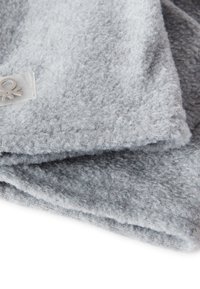 Couverture en polaire grise avec une surface douce et texturée. Présente une petite étiquette logo transparente sur le bord. Le matériau semble léger et confortable.