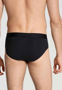 Schwarze Slips aus einem glatten, dehnbaren Stoff. Mit einem breiten Bund und einer enganliegenden Passform. Strukturierte Oberfläche am elastischen Band.