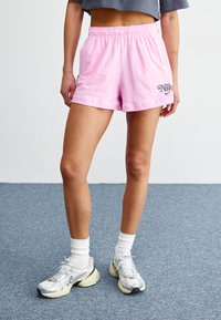 Rosa shorts med elastisk midja, med en Nike-logotyp i mörkgrått. Bärs med vita ankelsockor och grå sneakers med gula detaljer.