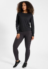 Czarna sportowa bluzka z długim rękawem o fakturowanej tkaninie; ciemnoszare legginsy z wzorem w jodełkę po bokach. W komplecie czarne buty sportowe.