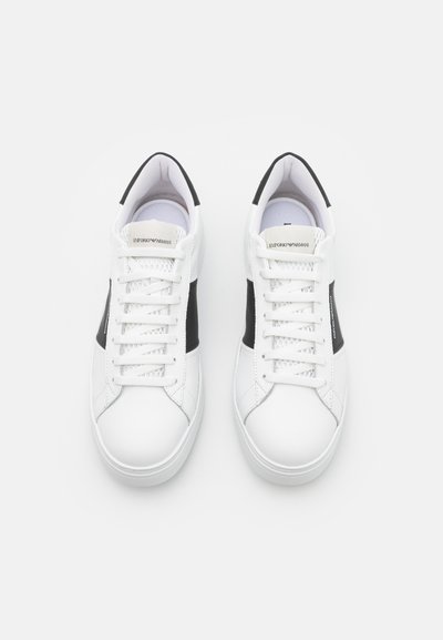 Vita sneakers med svarta sidodetaljer, runt tåparti och platt gummisula. Har snörning och ett märke på tungan.