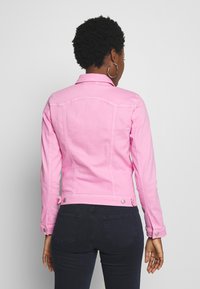 Chaqueta de mezclilla rosa con diseño entallado, botones decorativos y detalles de costuras visibles. Cuenta con mangas largas y cuello clásico.