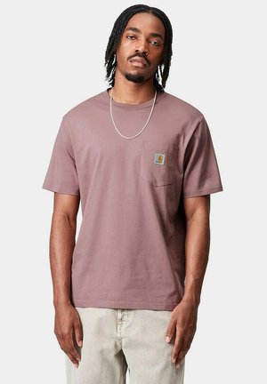 T-shirt di cotone a maniche corte color malva con tasca sul petto sinistro e patch con logo, abbinato a pantaloni chiari.