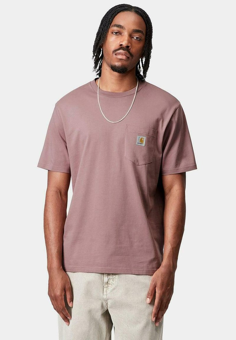 T-shirt di cotone a maniche corte color malva con tasca sul petto sinistro e patch con logo, abbinato a pantaloni chiari.