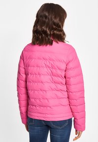 Roze pufferjack met een horizontaal gestikt patroon, hoge kraag en een gladde textuur. Draagt met blauwe jeans vanuit een achteraanzicht.