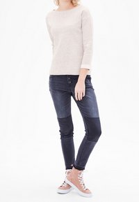 Pull beige texturé à manches trois-quarts, associé à un jean en denim foncé avec un design color block et des baskets montantes rose clair.