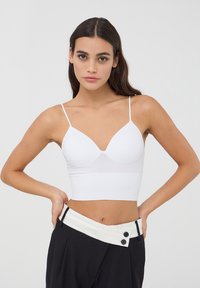Cropped top bianco a coste con spalline sottili e scollatura a V, caratterizzato da un design senza cuciture per un comfort ottimale e un aspetto liscio.