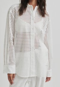 White button-up shirt with a grid pattern, featuring a lightweight fabric, long sleeves, and a relaxed fit. Ideal for layering or as a breathable option.