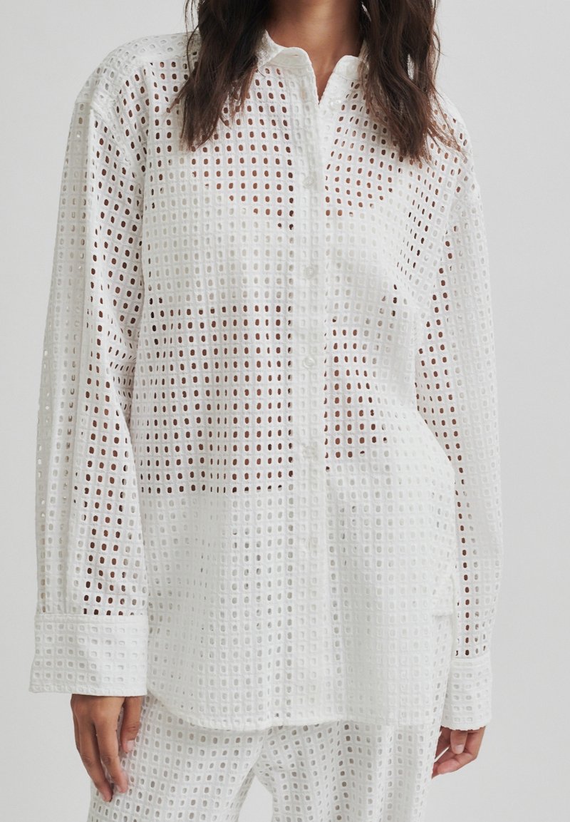 White button-up shirt with a grid pattern, featuring a lightweight fabric, long sleeves, and a relaxed fit. Ideal for layering or as a breathable option.