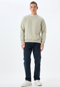 Sudadera gris clara con cuello redondo y mangas raglán, combinada con jeans azul oscuro y zapatillas blancas. Tela suave, corte casual.