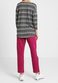Langermige zwart-wit patroon top gecombineerd met roze broek. De outfit heeft een ontspannen pasvorm en contrasterende kleuren. Witte sneakers inbegrepen.