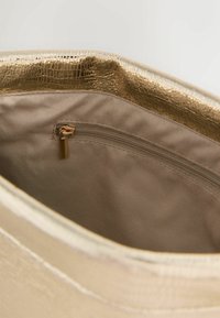 Metallic-goldene Handtasche mit strukturierter Außenseite. Das Innere verfügt über ein glattes, beiges Futter und eine Reißverschlusstasche für sichere Aufbewahrung.