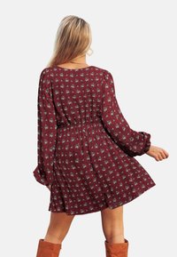 Bordeauxfarbenes Blumenmusterkleid mit langen Ärmeln, elastischem Bund und schwingendem Rock, das mit einem kleinen weißen Blumenmuster und weichem Stoff versehen ist.