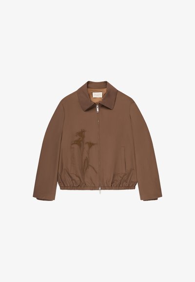 Giacca marrone con zip, collo, vita elastica e due tasche laterali, mostrata su sfondo bianco.