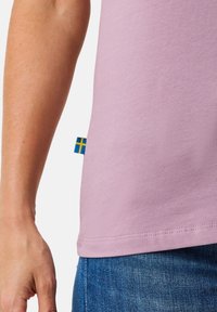 Lyserød bomulds T-shirt med rund halsudskæring, korte ærmer og et lille blå-gult flagmærke på side sømmen.
