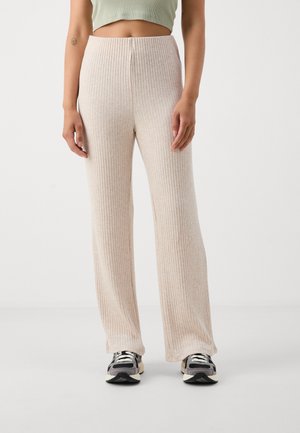 Pantalons larges beige à côtes avec taille haute, présentant une texture douce et une coupe droite, associés à des baskets noires et beiges.