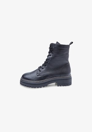 Mustat nahkasaappaat, joissa on nyöritys nilkkamittaisena, teksturoitu pinta, paksu kumipohja ja kontrastiväri valkoisella ompelulla pohjan ympärillä.