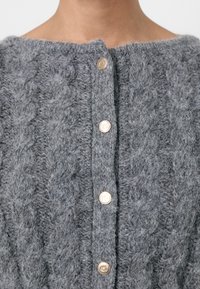 Gilet en tricot gris à mailles, avec une surface texturée, doté d'un col rond et de boutons métalliques à l'avant.