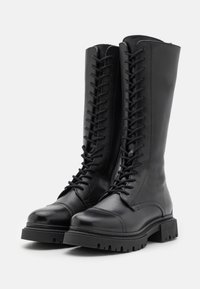 Černé kožené šněrovací vysoké boty po kolena s kulatou špičkou, zesílenou špičkou, masivní podrážkou a vertikálním švem.