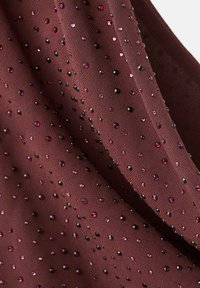 Bordová tkanina s textúrovaným povrchom, zdobená roztrúsenými ružovými a čiernymi rhinestone-kameňmi, vytvárajúcimi lesklý vzor.