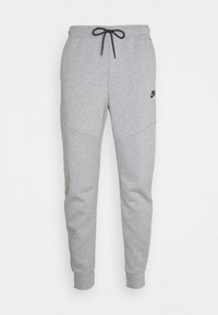 Šedé tepláky se stahovací šňůrkou v pase, s hladkou texturou, zúženými nohavicemi a malým černým logem Nike na levém stehně.