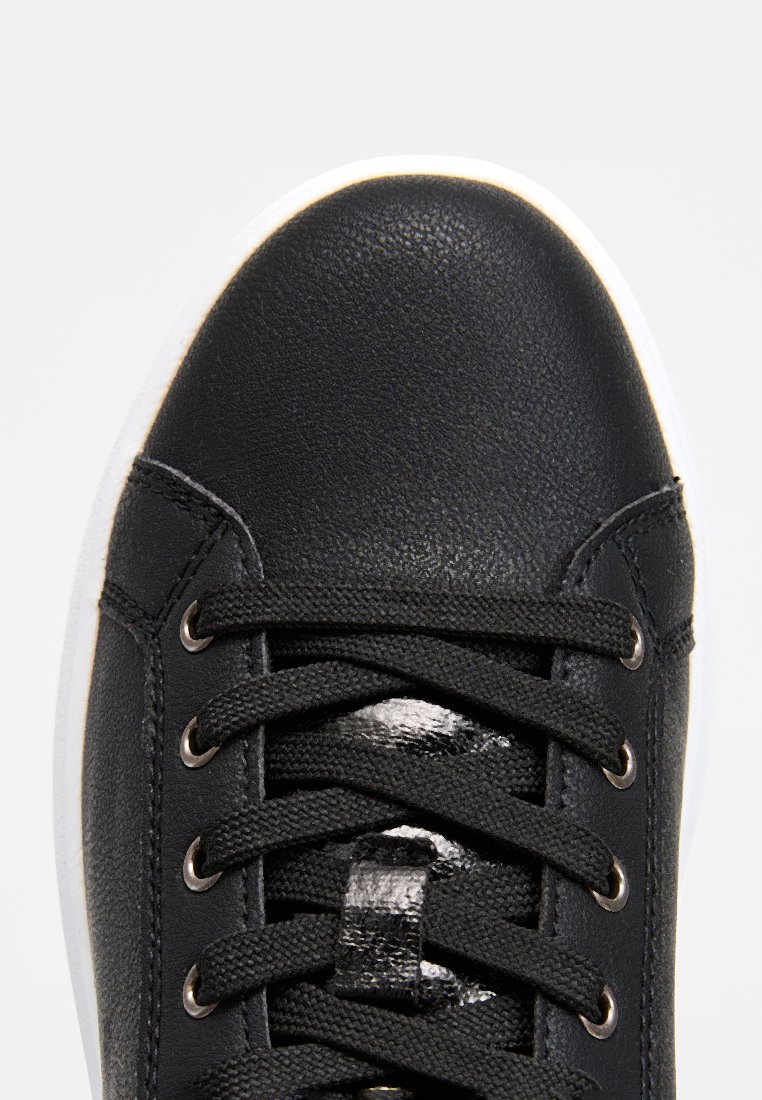 Basket noire avec un upper en cuir texturé, bout rond et semelle en caoutchouc blanche. Dispose de lacets noirs et d'œillets métalliques.