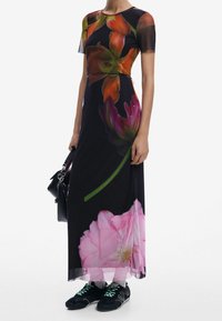 Robe maxi avec un motif floral aux couleurs vives sur un fond noir. La robe a des manches courtes et une coupe ajustée, associée à des baskets noires.
