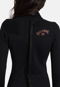 Mutino nero con colletto alto, chiusura a zip e logo Billabong color ruggine. Texture liscia e design sagomato per una vestibilità aerodinamica.
