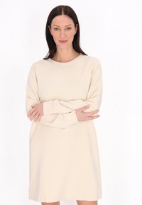 Beige, hosszú ujjú ruha átlós textúrával, kerek nyakkivágással és laza illeszkedéssel, amely a comb közepéig ér.
