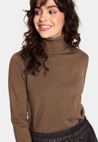 Brauner Rollkragenpullover mit langen Ärmeln, aus weichem geripptem Stoff, in taillierter Passform. Kombiniert mit einem strukturierten schwarzen Bund.