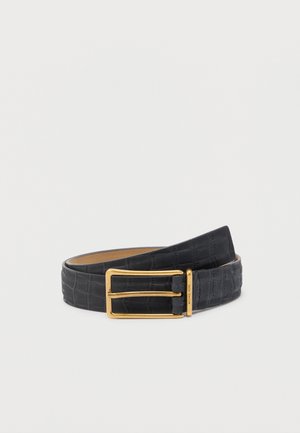 Črni usnjeni pas s teksturo krokodila in zlatim pravokotnim zaponko, zvit na enostavni svetlo sivi podlagi.