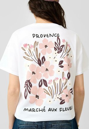 Person trägt ein weißes Hemd mit pinken Blumen- und Blattmotiven und dem Text "Provence Marché Aux Fleurs" auf dem Rücken.