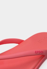 Κοντινή λήψη ενός ροζ κοραλλί σαγιονάρου Crocs που δείχνει την υφή της σόλας και το λογότυπο στο λουράκι σε λευκό φόντο.