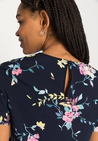 Vestido azul marinho com mangas curtas, apresentando flores brilhantes em rosa e amarelo, e um pequeno detalhe de botão em forma de chave nas costas.