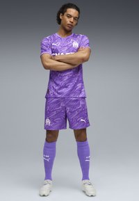Uniforme da calcio viola con un motivo a spirale, composto da una maglietta a maniche corte e pantaloni corti, abbinato a calze al ginocchio e scarpe da calcio.