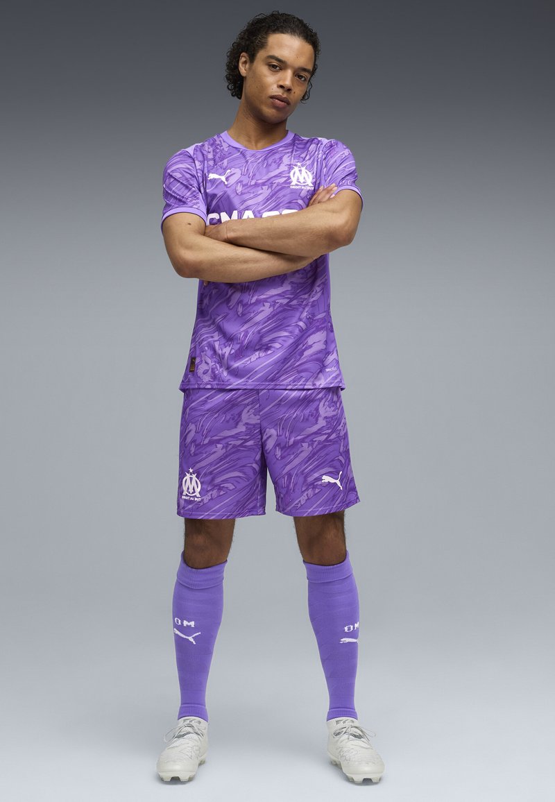 Uniforme da calcio viola con un motivo a spirale, composto da una maglietta a maniche corte e pantaloni corti, abbinato a calze al ginocchio e scarpe da calcio.