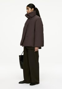 Brown puffer jacket with high collar, button closure, and oversized fit. Paired with wide-leg dark pants and a textured black tote bag.