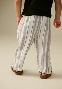 Weiße Leinenhosen mit blauen vertikalen Streifen, lockere Passform, ausgestattet mit einem bequemen Bund und braunen Sandalen mit Riemen.