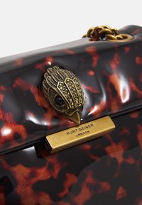 Handväska med sköldpaddsdesign som har en gyllene kedja och ett fågelformat lås med svarta stenar. Graverad varumärkesetikett.