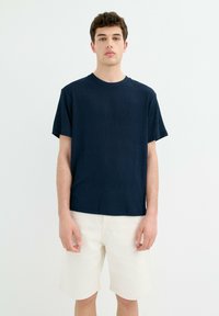 Camiseta de rayas navy con mangas cortas y cuello redondo, combinada con shorts blancos. La tela tiene una apariencia suave y texturizada.
