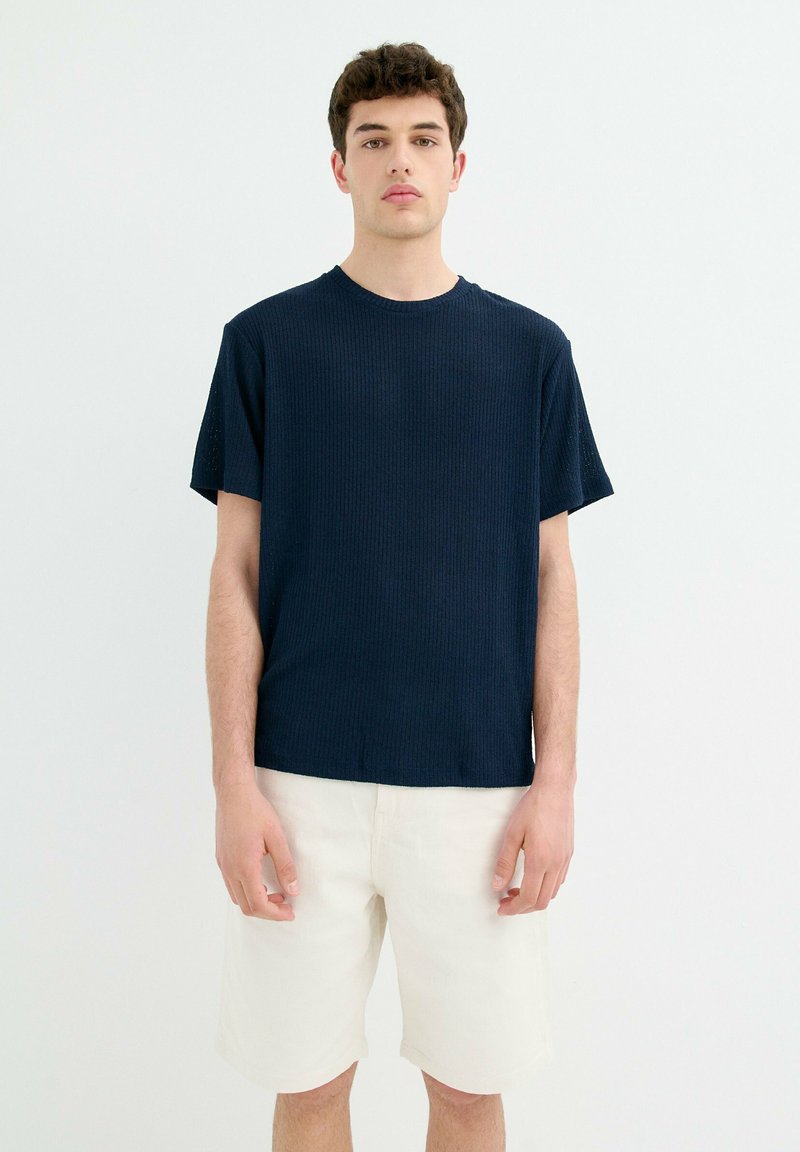 Camiseta de rayas navy con mangas cortas y cuello redondo, combinada con shorts blancos. La tela tiene una apariencia suave y texturizada.