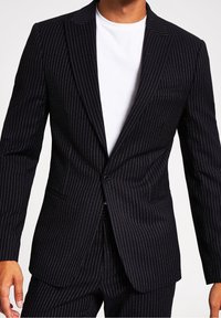 Mörkblå blazer med smårandigt mönster, enstaka knappstängning, slagkrage och bröstficka. Bärs över en vit t-shirt med rund halsringning.