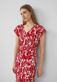 Rot-weiß gemustertes Kleid mit kurzen Ärmeln, V-Ausschnitt, tailliertem Bund, das abstrakte Blättermuster und eine fließende Silhouette zeigt.