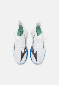 Le scarpe da corsa presentano una tomaia in mesh bianco con accenti neri, una suola blu e un dettaglio verde sulla parte del tallone. I lacci sono bianchi con una finitura testurizzata.