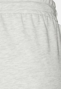 Světle šedé tepláky vyrobené z měkké, strukturované látky. Mají elastický pas a na bocích nazbíraný materiál, s hladkým, neutrálním vzhledem.