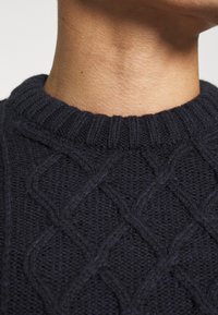 Pull en maille bleu marine avec un motif torsadé texturé, doté d'un col rond côtelé et d'un tissu doux et épais.