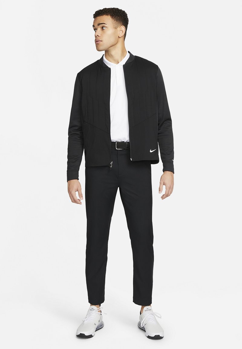 Sort nylon bomberjakke med lynlås, teksturerede paneler og et lille hvidt Nike-logo. Sættes sammen med sorte slim-fit bukser og hvide sneakers.