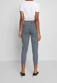 Czarno-białe spodnie w kratkę o slim fit i elastycznym pasie, połączone z gładką, białą bluzką z krótkim rękawem i czarnymi trampkami.