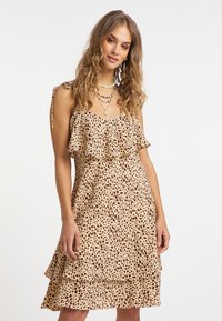 Leopardskinmönstrad klänning i ljusbrunt med volanger, justerbara knytband och en flödande silhuett. Mjuk tyg med en texturerad mönstring.